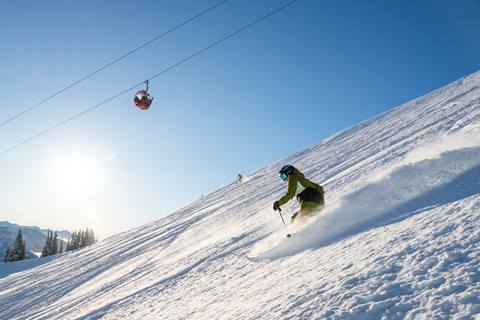 Two skiers ski down a bowl underneath a gondola on a bluebird day. 