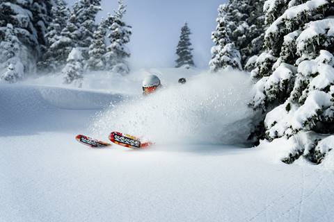 Skier glides through untouched powder with K2 ski ski tips poking out of the deep. 