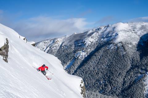 Skier with perfect form takes a right turn on a steep couloir with a beautiful view in the background. 