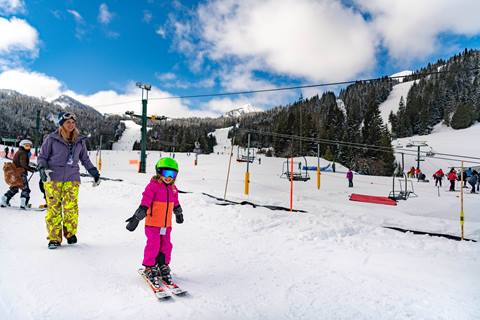 A young skier joyfully gets their first turns as their parent watches pridefully. 